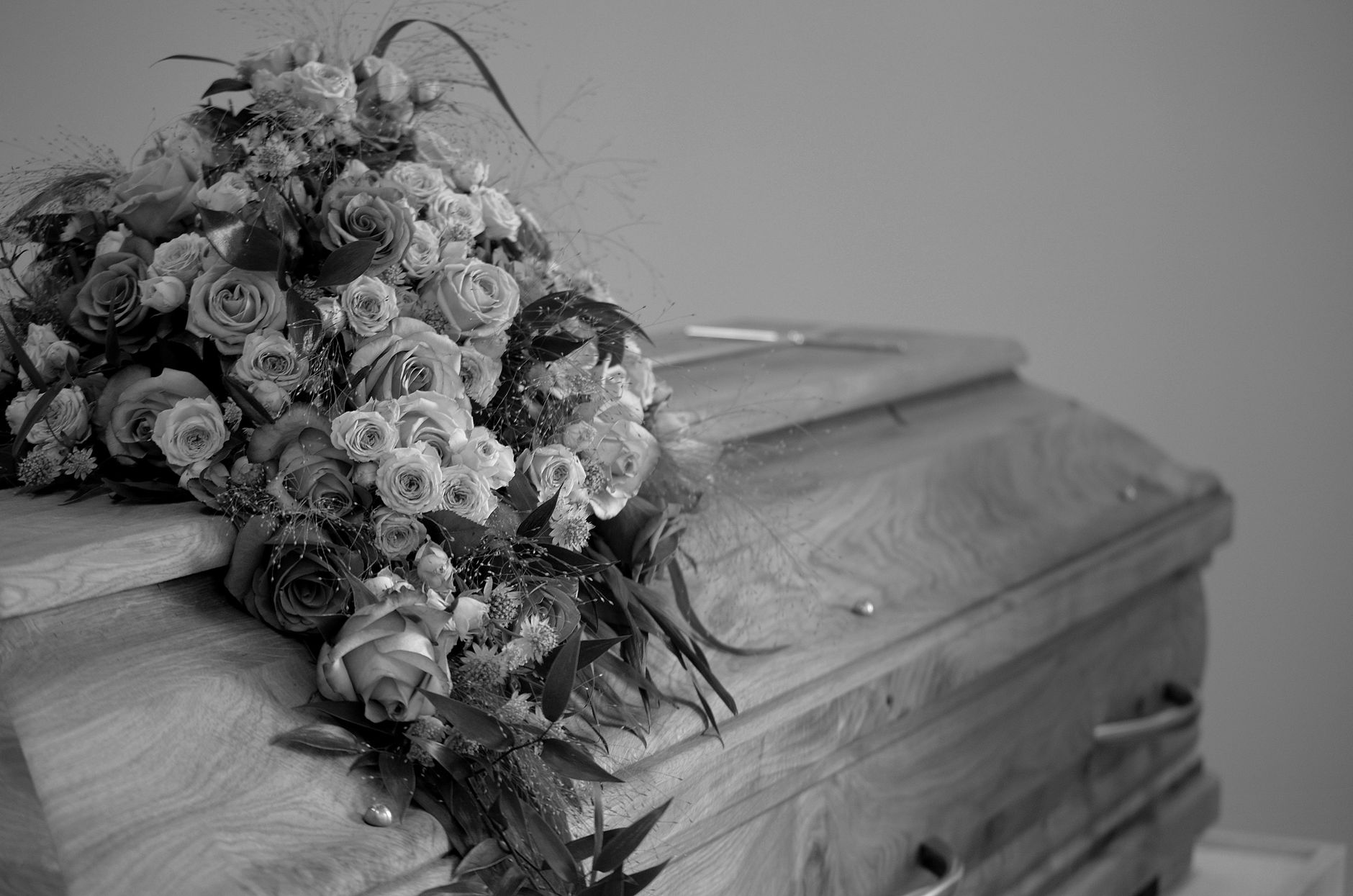 A casket adorned with a full arrangement of roses and white flowers